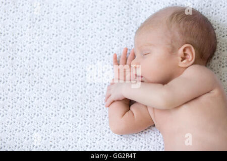Portrait of young funny newborn babe napping on white knitted blanket. Cute caucasian new born child sleeping. Healthy one month Stock Photo