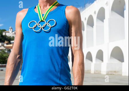 RIO DE JANEIRO - MARCH 6, 2015: Athlete wearing Olympic rings gold medal stands outdoors in front of the Lapa Arches. Stock Photo