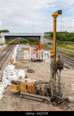 Construction workers, and pile drilling machine, on site next to a section of railway track. In Ilkeston, Derbyshire, England. Stock Photo