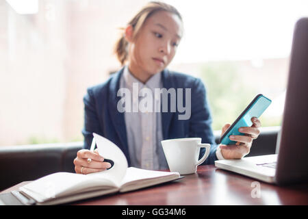 Young woman using mobile phone while studying Stock Photo