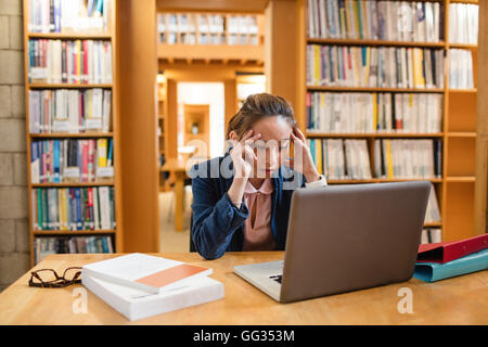 Tensed young woman using laptop in library Stock Photo
