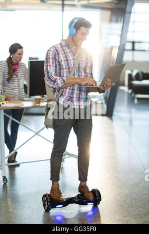 Smiling man standing on hoverboard and using laptop Stock Photo