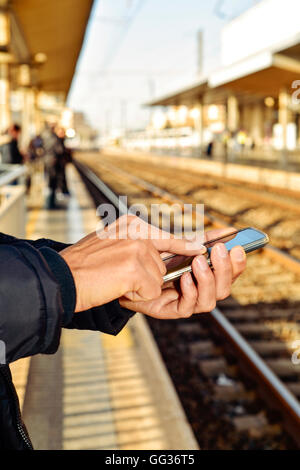 closeup of a young caucasian man using a smartphone in an open-air train station or tram station Stock Photo