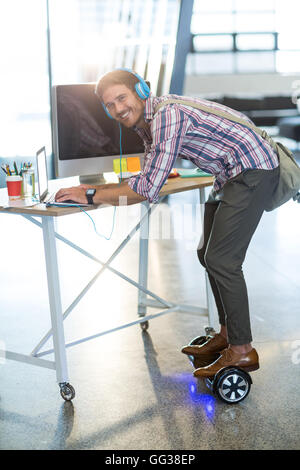 Smiling man standing on hoverboard and using laptop in office Stock Photo