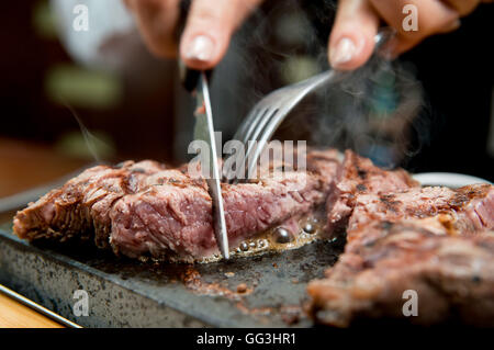 Rib eye steak being cooked and cut on a hot stone in a restaurant Stock Photo