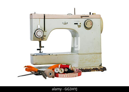 Old rusty vintage sewing machine with cotton reels, grungy scissors and tape measure on white background Stock Photo