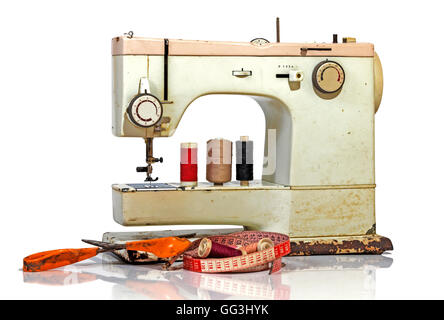 Old rusty vintage sewing machine with colored cotton reels, scissors tape measure and old scissors on white background Stock Photo