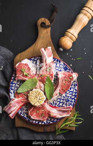 Raw uncooked lamb chops with herbs and spices on wooden board over dark  background Stock Photo