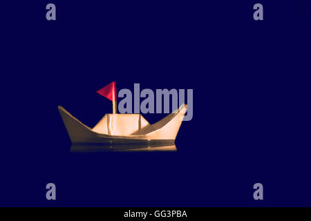ghostly paper boat floating in water on blue background with red flag Stock Photo
