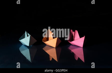 three ships of different colored paper on blue and black background Stock Photo