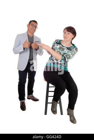 A unhappy middle age woman sitting on a chair pointing her finger at her husband, he is smiling, isolated for white background. Stock Photo