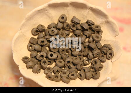 Hand Made Clay Beads. Group of handmade ceramic beads made of wet black clay in natural matte finish,after punching holes stacked  in a clay dish. Stock Photo