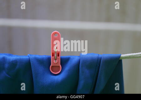 Blue Laundry Drying. Blue Shorts hanging on a clothes line with single red clothespin, plastic laundry stick. Sun drying  - green housekeeping. Stock Photo