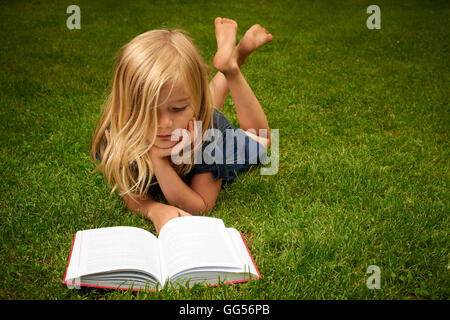 Cute Little Blond Girl Reading Book Outside on Grass Stock Photo