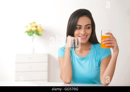 Beautiful young woman holding glass of fresh orange juice at home Stock Photo