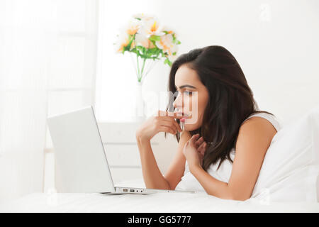 Side view of young woman using laptop in bed Stock Photo
