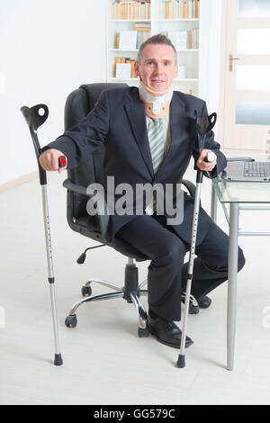 Businessman at work wearing neck brace with crutches Stock Photo