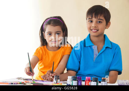 Portrait of siblings painting at table against colored background Stock Photo