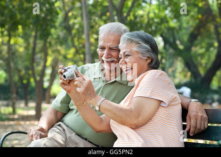 Cheerful couple using digital camera at park Stock Photo