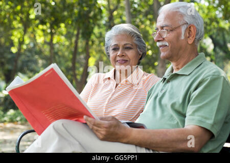 Relaxed senior man reading book with woman at park Stock Photo