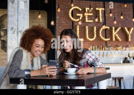 Female friends using a smart phone with coffee at cafe Stock Photo