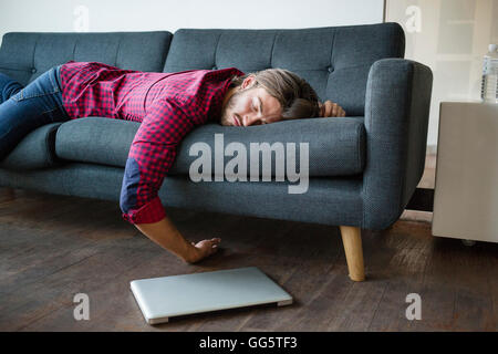 Young man sleeping on sofa with laptop Stock Photo