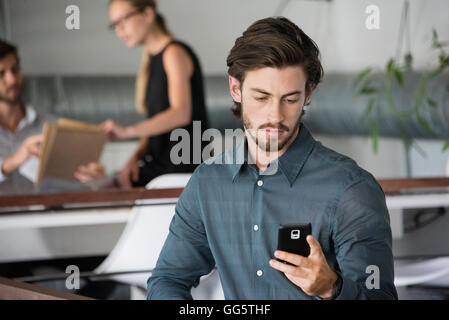 Businessman using a smart phone with his colleagues in the background Stock Photo