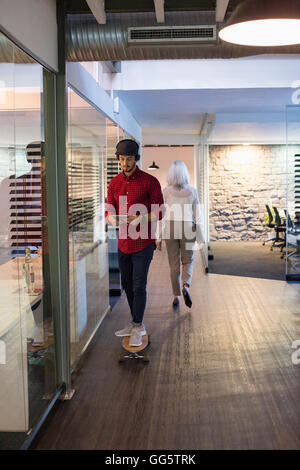 Young man using a digital tablet on skateboard with colleague in office hallway Stock Photo