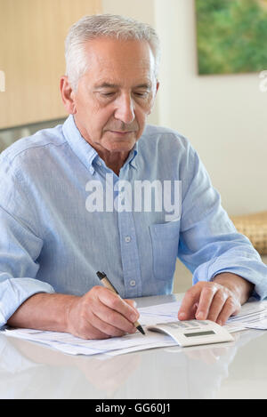 Senior man using a calculator while doing paperwork at home Stock Photo
