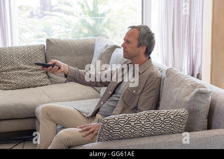 Man using remote control on couch in a living room Stock Photo