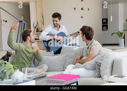 Happy man playing a guitar with his friends sitting near him Stock Photo