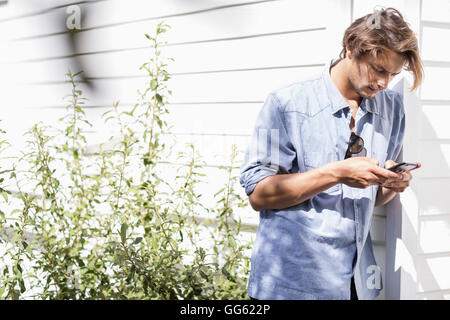 Young man using smartphone leaning against wall Stock Photo