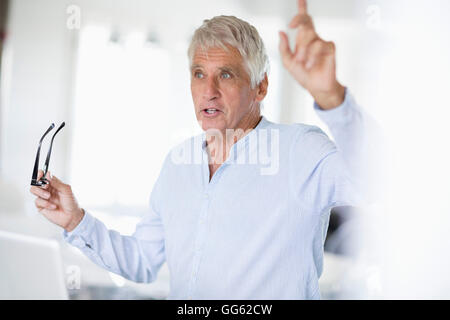 Senior man gesturing with laptop on table Stock Photo