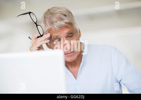 Worried senior man head in hand with laptop on table Stock Photo