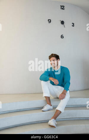 Happy young man sitting on steps at home Stock Photo