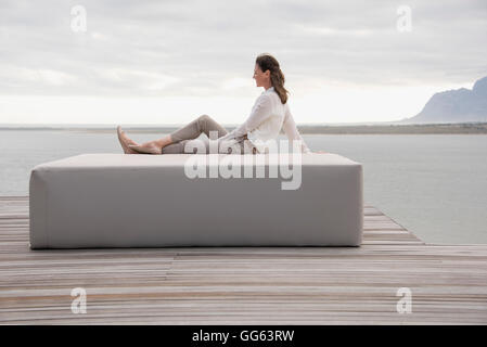 Side profile of a mature woman sitting on ottoman at lakeshore Stock Photo