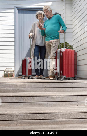 Senior couple with suitcase using smartphone at front door Stock Photo