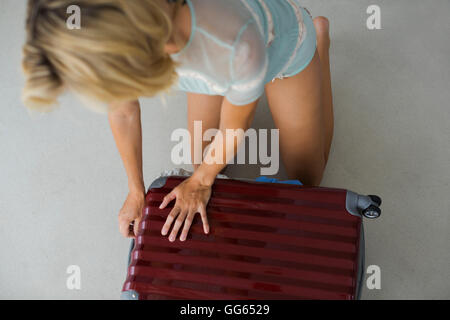 Young woman trying to close overflow suitcase Stock Photo