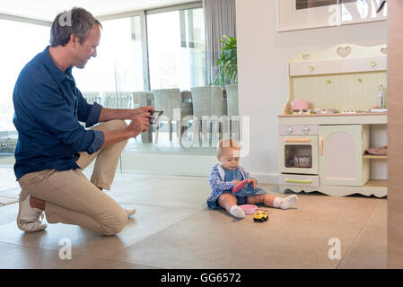 Mature man taking picture of her baby daughter playing with toys Stock Photo