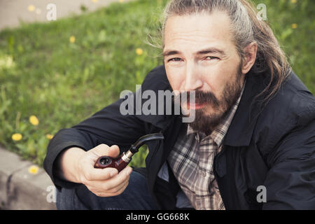 Asian man smoking a pipe on green grass in park, close-up photo with selective focus Stock Photo