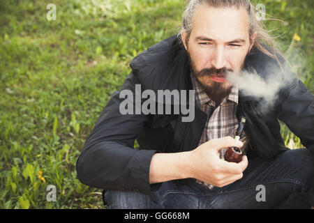 Asian man smoking a pipe on green grass in park, closeup photo with selective focus Stock Photo