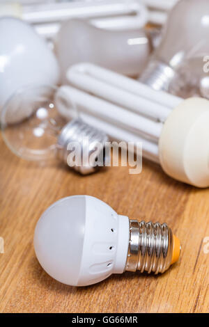 new LED lamp and pile of old incandescent light bulbs and used compact Fluorescent lamps on wooden board Stock Photo