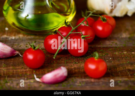 closeup of some cherry tomatoes, some garlic cloves and a glass cruet with olive oil on a rustic wooden table Stock Photo