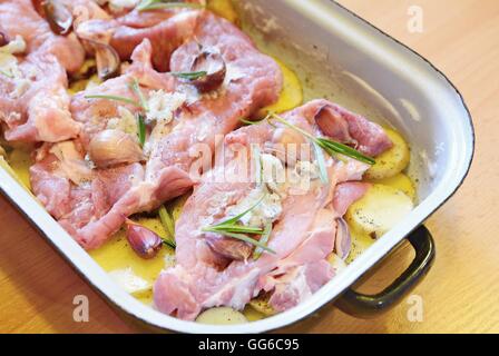 Raw pork neck chops with potatoes slices, rosemary and garlic in pan. The meal is prepared for baking. Stock Photo