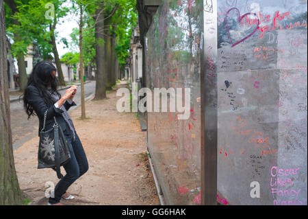 Paris Pere Lachaise, visitor to the tomb of Oscar Wilde in the Pere Lachaise Cemetery photographs graffiti on the perspex screen around the grave. Stock Photo