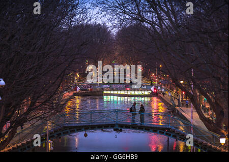 Paris winter night, view of two young people standing on a bridge over the Canal Saint-Martin on a winter evening, central Paris, France. Stock Photo