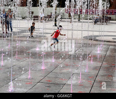 young boy runs through illuminated pavement jets of water fountain in public square Skopje Macedonia Stock Photo