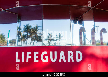 Lifeguard lookout tower office red building on beach ocean pools with reflective glass of trees blue sky. Stock Photo