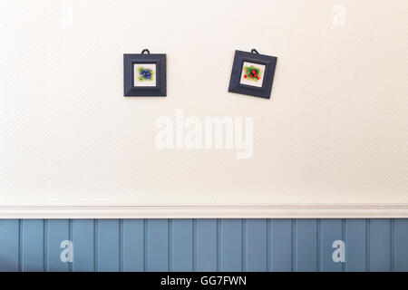 Two small square pictures of blueberries and strawberries in frames hanging on the white blue wall. Stock Photo