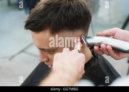 Professional styling. Close up side view of young man getting haircut by hairdresser with electric razor at barbershop Stock Photo